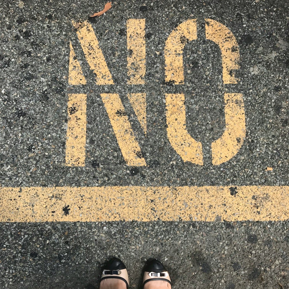 person wearing black leather shoes standing on gray concrete pavement with yellow and black i love