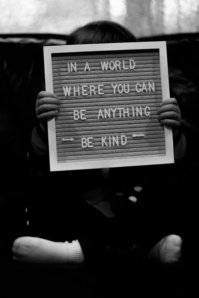 Child holds letter board with "be kind" message.