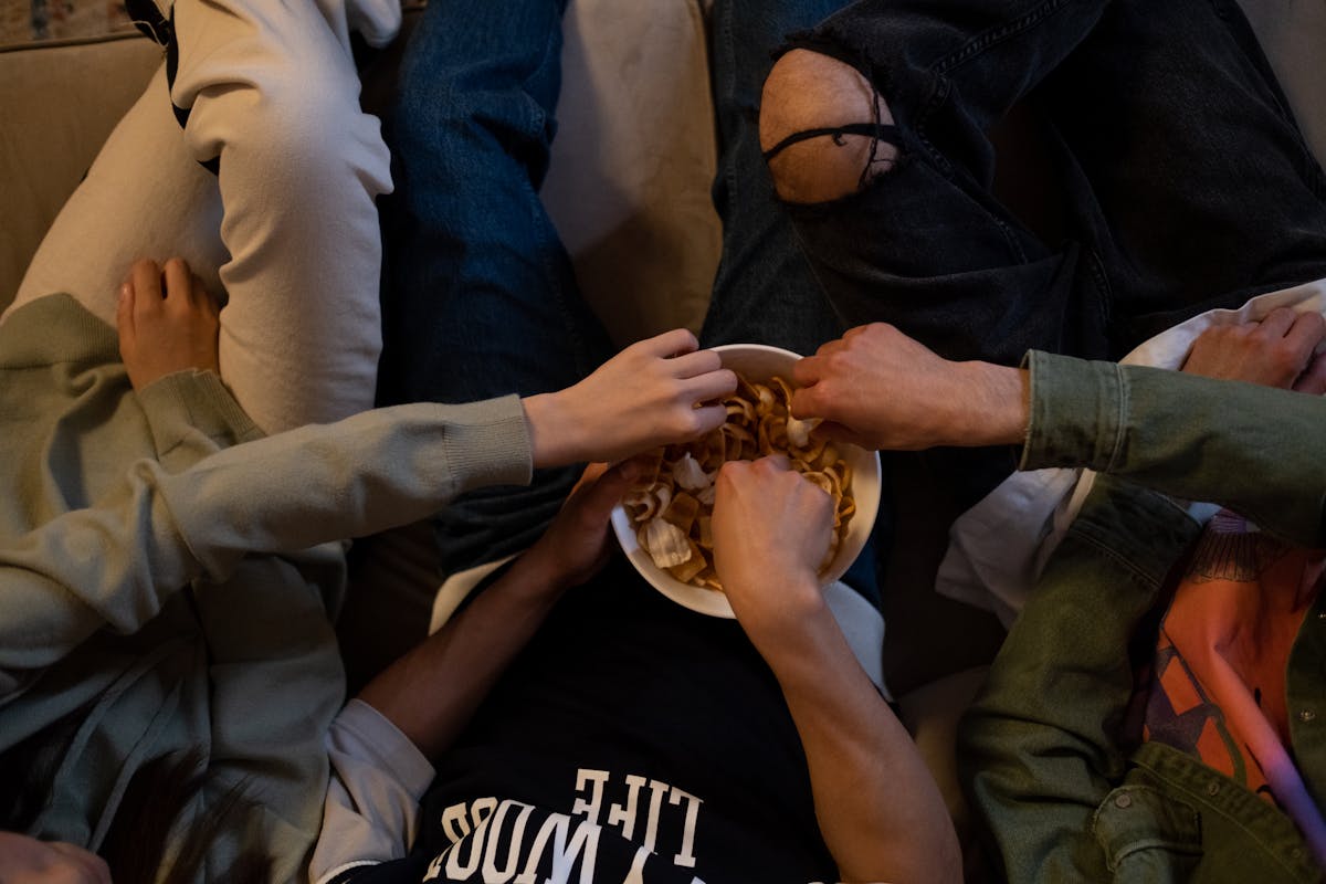 Close-up of friends reaching for snacks during a cozy movie night indoors.