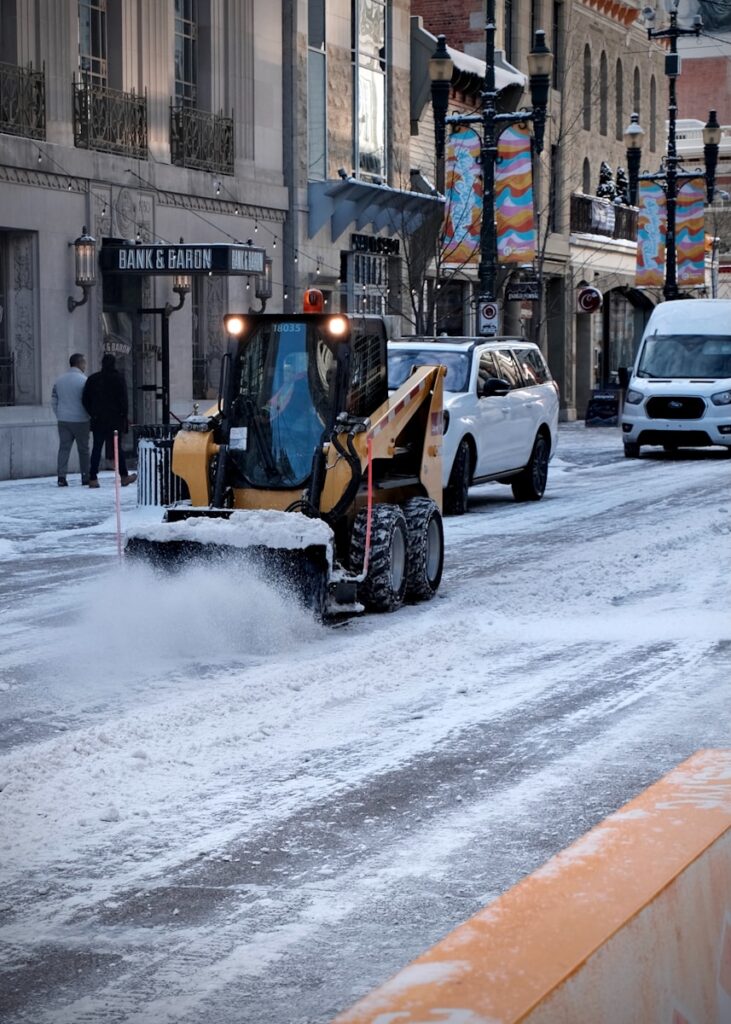 Skid steer loader plowing snow on a city street.