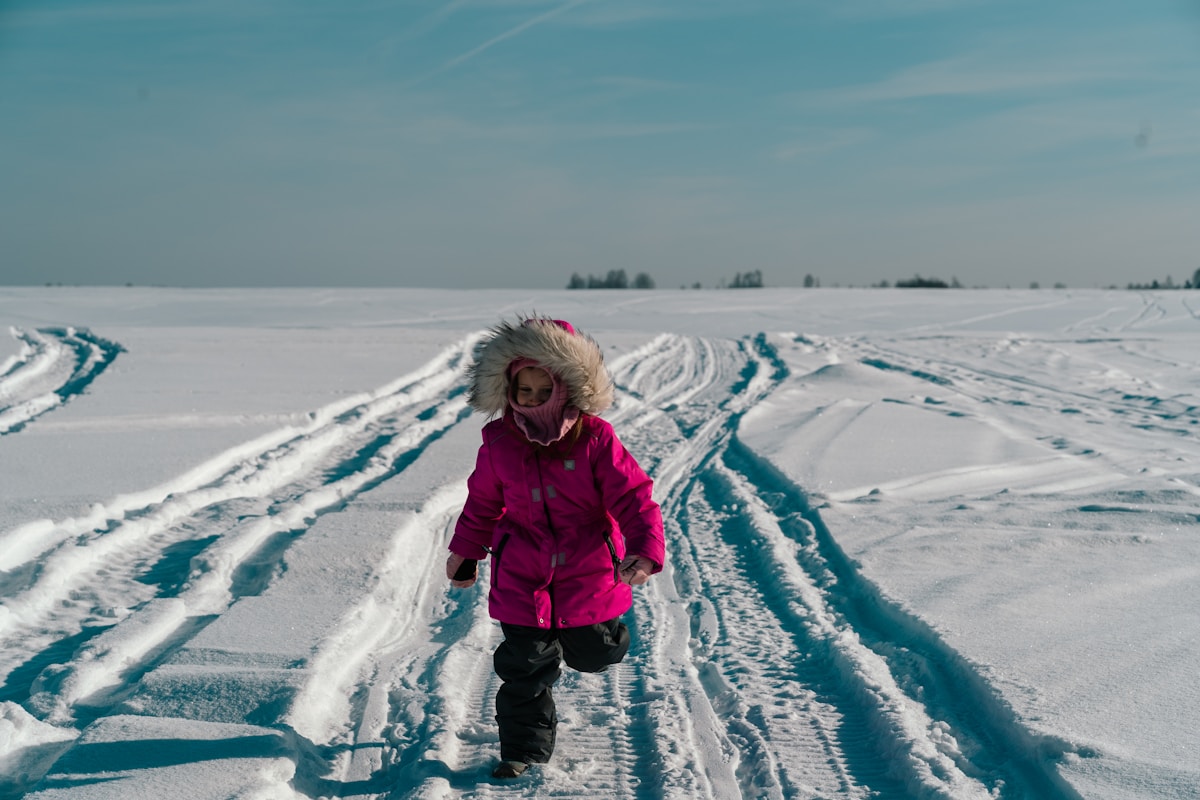 a little girl in a pink coat is walking in the snow