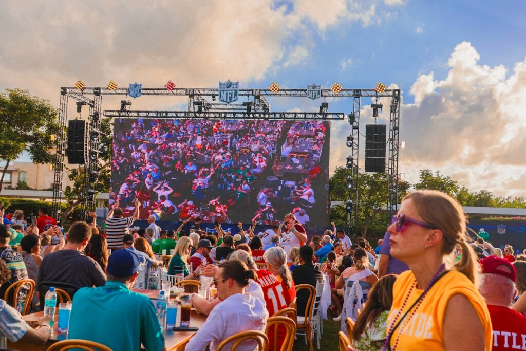 A large group of people sitting at tables in front of a large screen