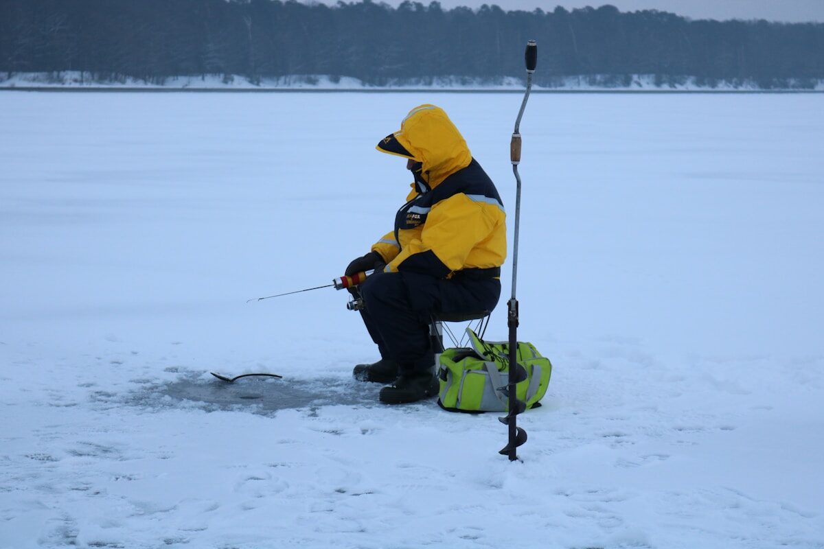 a man in a yellow jacket fishing on a frozen lake