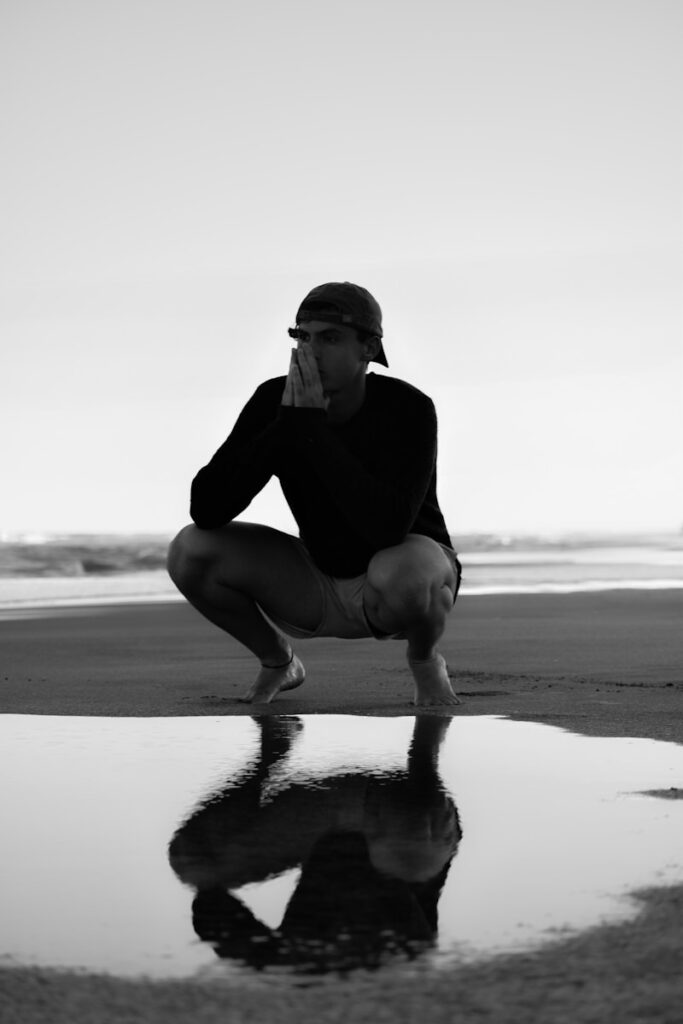 a man kneeling down on a beach next to a body of water