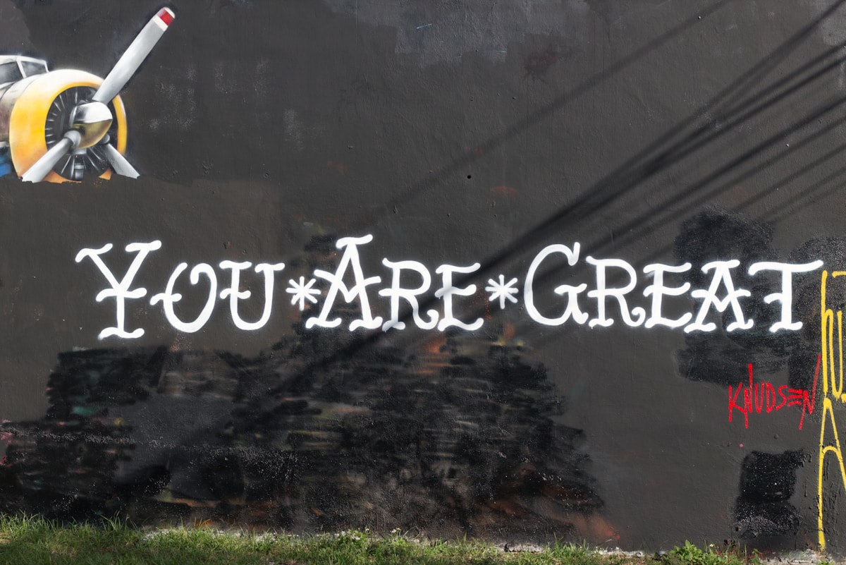 Propeller plane flies over "you are great" mural.