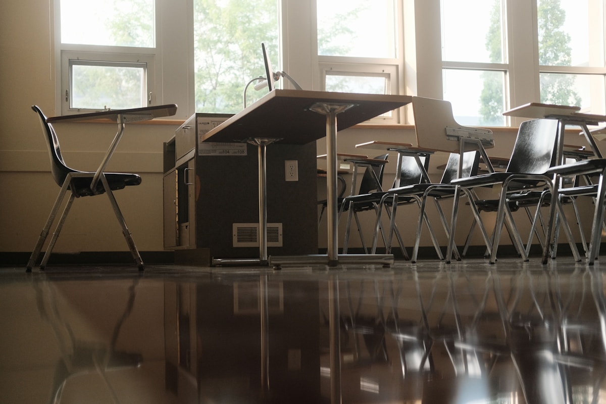 Empty classroom with desks and chairs by windows.